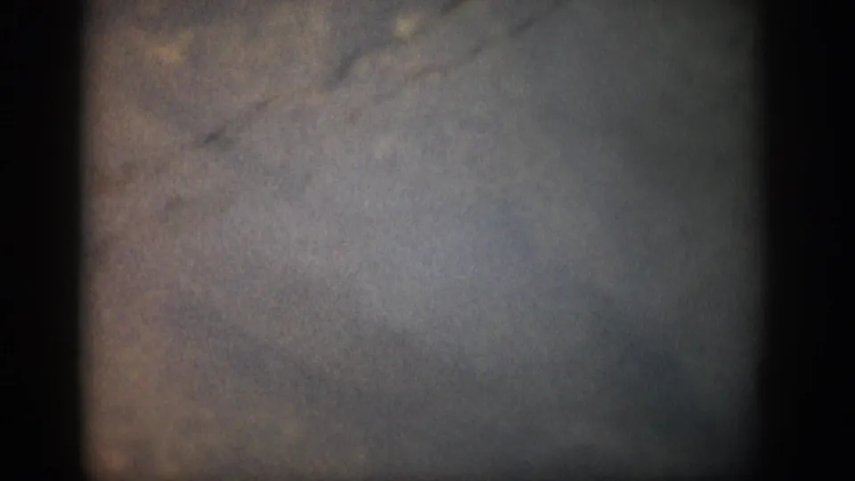 Opening 8mm frame from the Colorado 1959 clip showing mostly dark, mottled exposure before the stream scene appears.