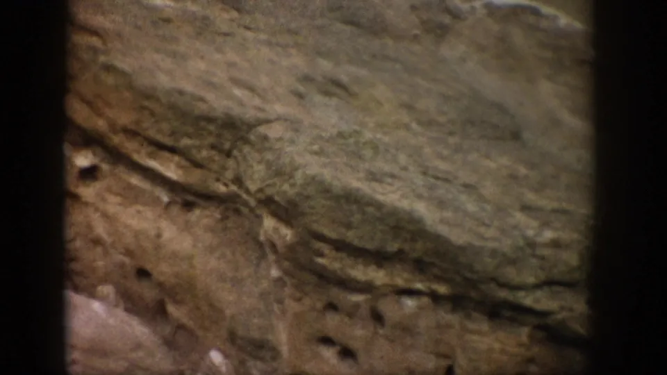 1959 Colorado home-movie frame showing a sloped sandstone layer, pitted rock face, and visible 8mm edge darkness.