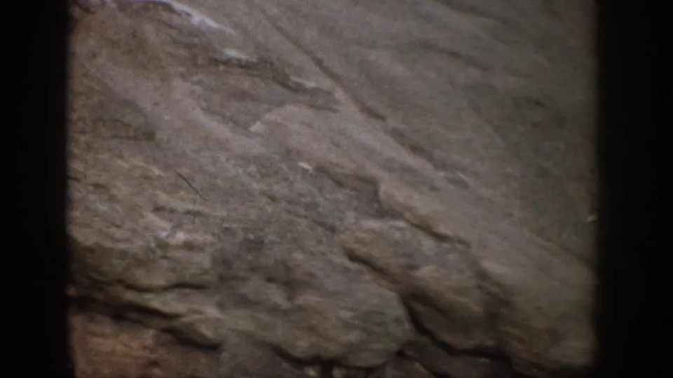 1959 Colorado 8mm frame showing a close, soft-focused view of rough layered rock and sediment-like surface texture.