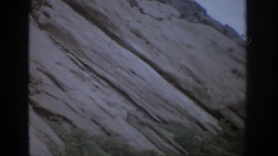 1959 Colorado 8mm frame showing diagonal pale rock layers, dark film borders, and small vegetation at the lower edge.