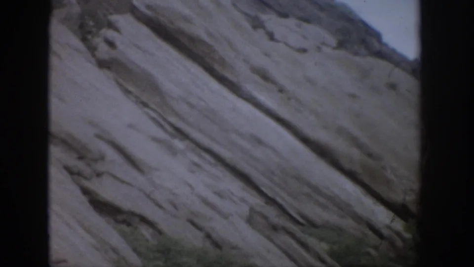 1959 Colorado 8mm frame showing a steep diagonal rock formation with layered lines and a narrow strip of vegetation below.