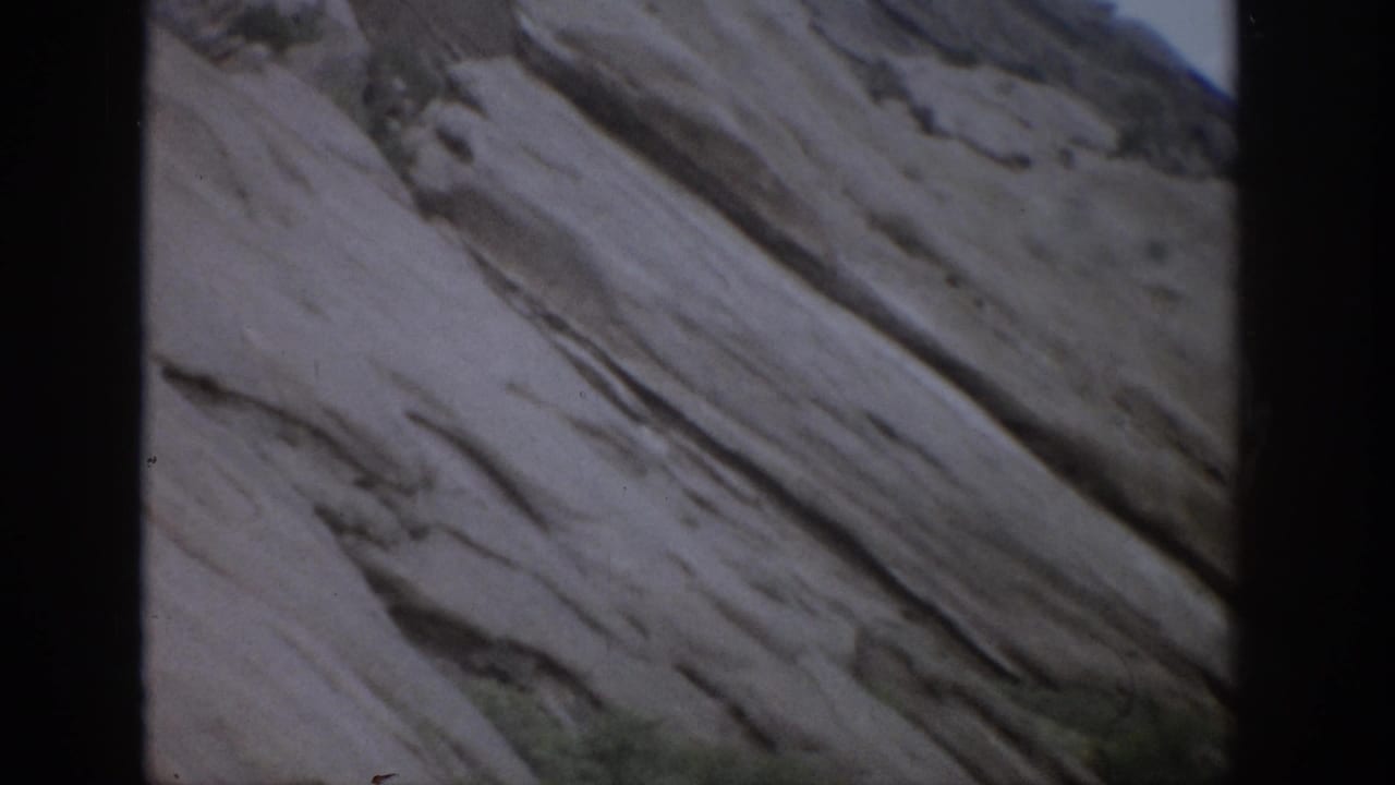 1959 Colorado 8mm frame showing a close view of pale layered rock with diagonal strata and a narrow strip of sky.