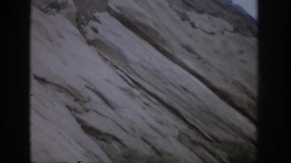 1959 Colorado 8mm frame showing a close view of pale layered rock with diagonal strata and a narrow strip of sky.