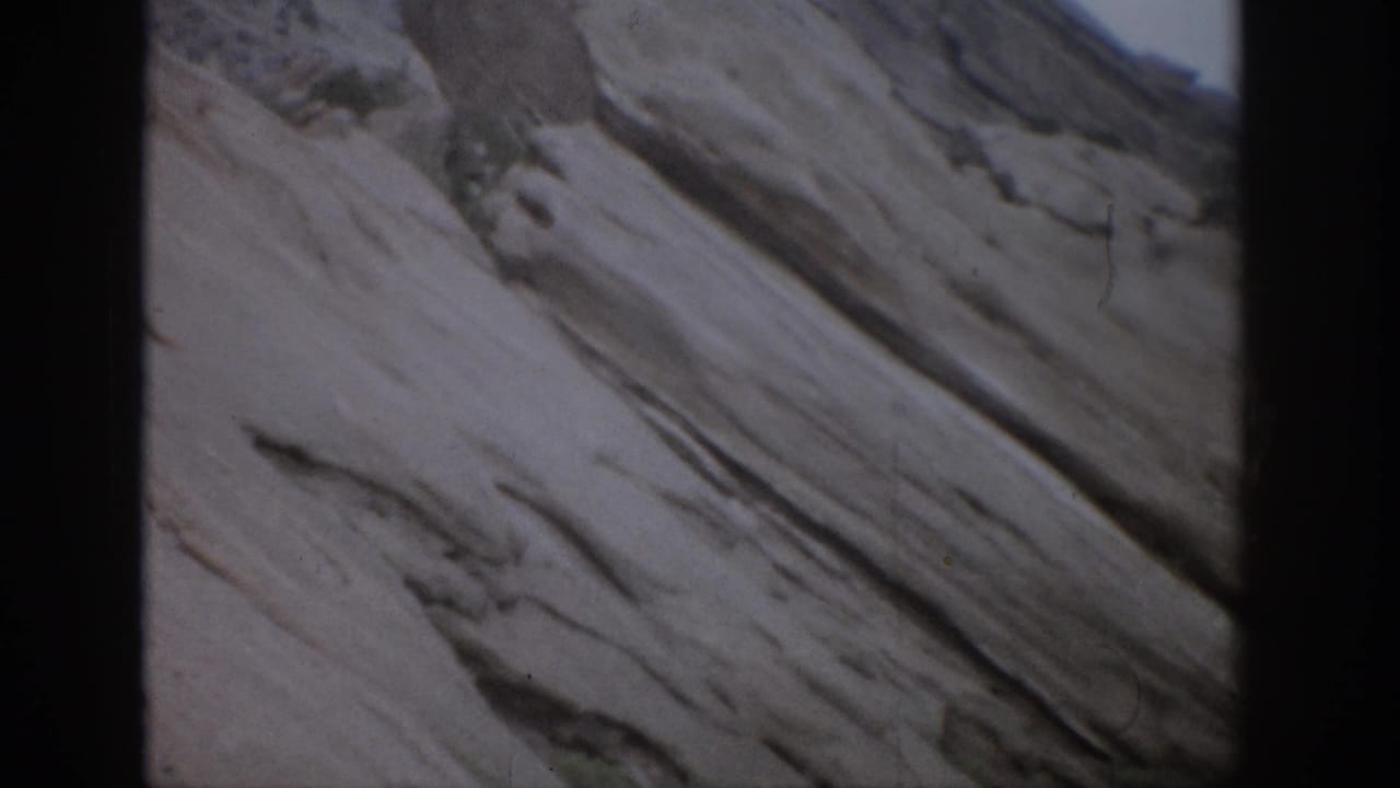 Pale mountain rock face with long diagonal grooves and dark borders.
