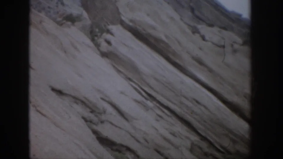 1959 Colorado 8mm frame with a rugged rock wall, diagonal stone layers, and faint vegetation near the lower edge.