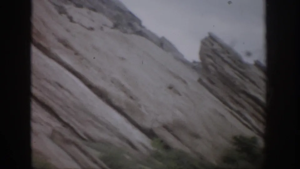 1959 Colorado 8mm frame showing angled rock formations, pale sky along the upper edge, and low green shrubs below.