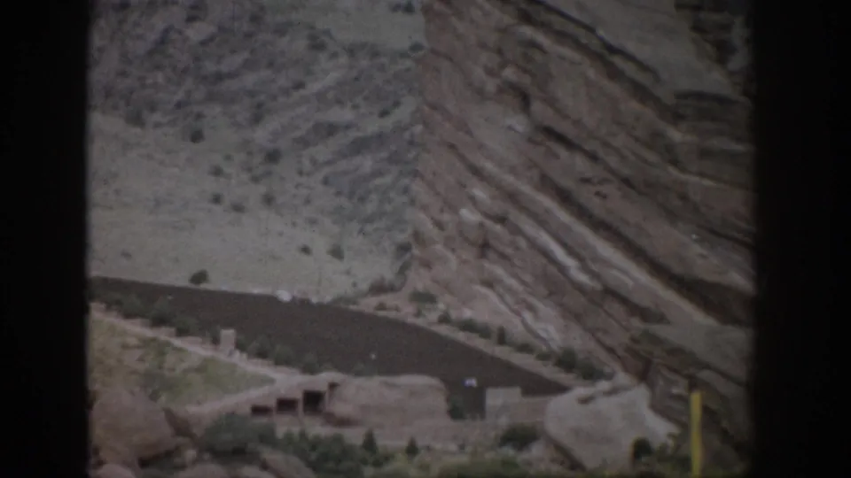 Colorado 1959 8mm view of angled sediment-like layers, sparse shrubs, and a road cutting across the base of the slope.