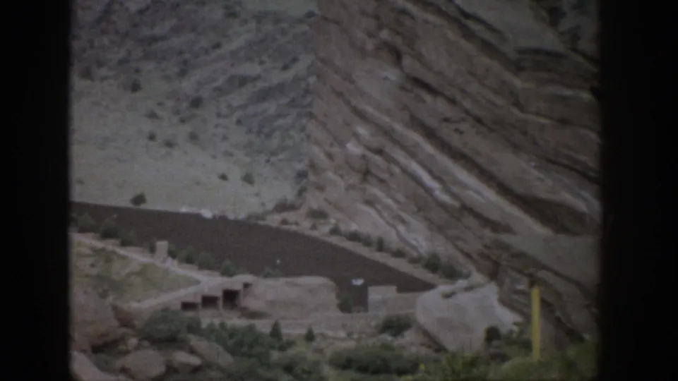 1959 Colorado home-movie frame showing distant cliff dwellings and a layered sandstone wall through a dark foreground frame.
