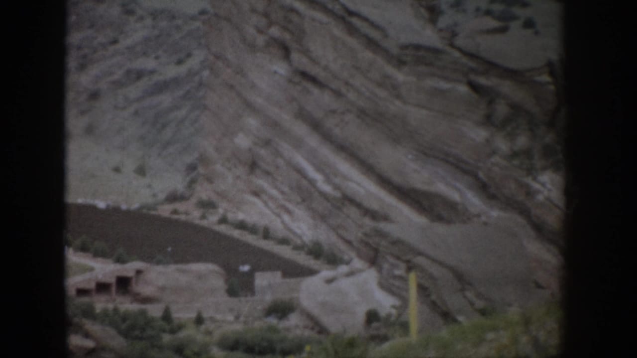 A 1959 Colorado view holds on cliff dwellings against banded sandstone, partially divided by a dark foreground bar.