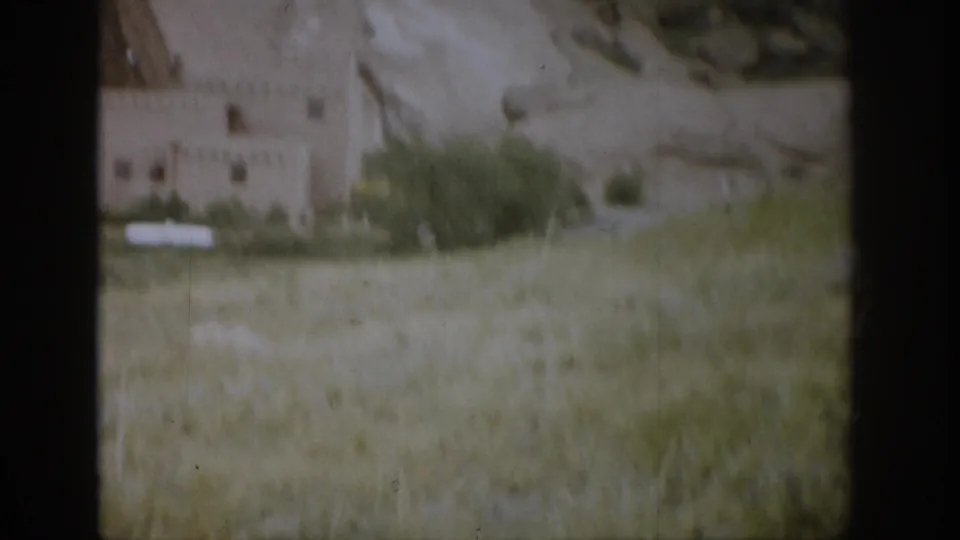 1959 Colorado footage shows an adobe-style structure with small windows below sandstone cliffs and grassy foreground.