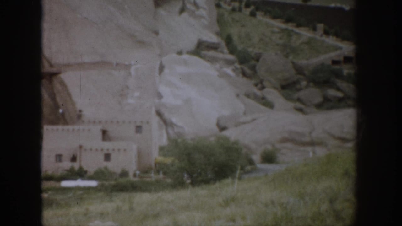Colorado home-movie view of an adobe-style exterior set against rugged pale rock, with vegetation and dark 8mm frame edges.