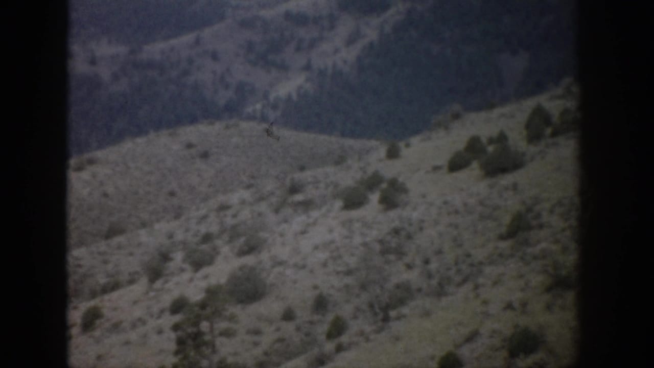 1959 Colorado home-movie frame showing arid rolling hills, sparse vegetation, and distant ridges with visible 8mm frame edges.