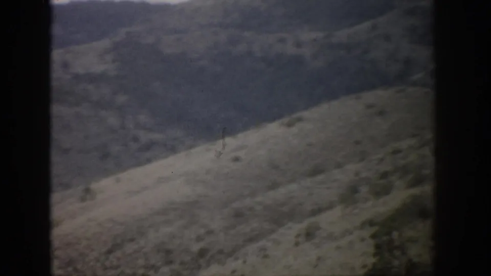 Soft 8mm frame from 1959 Colorado showing a sloped arid hillside, brush, and darker mountain terrain beyond.