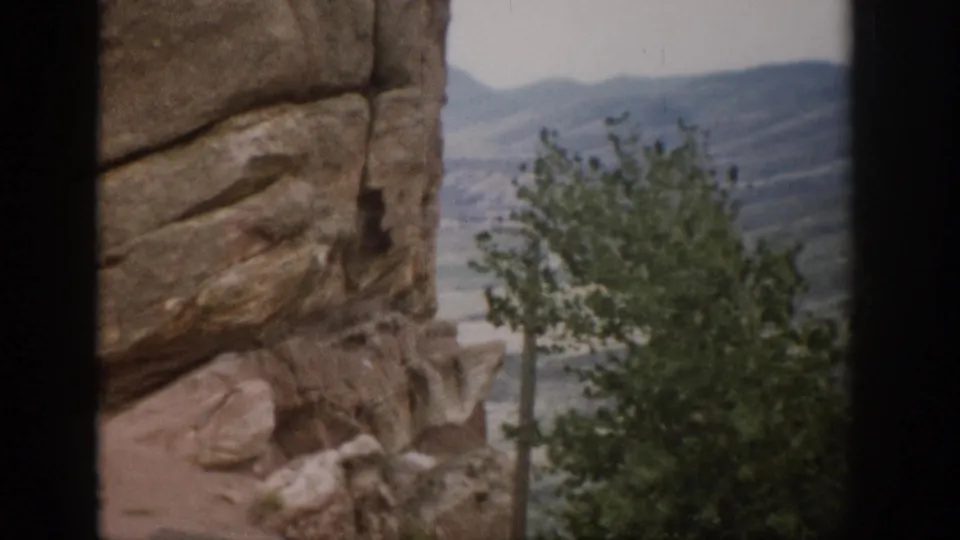 Colorado 8mm frame showing a textured rock formation, foreground tree, and soft distant hills.