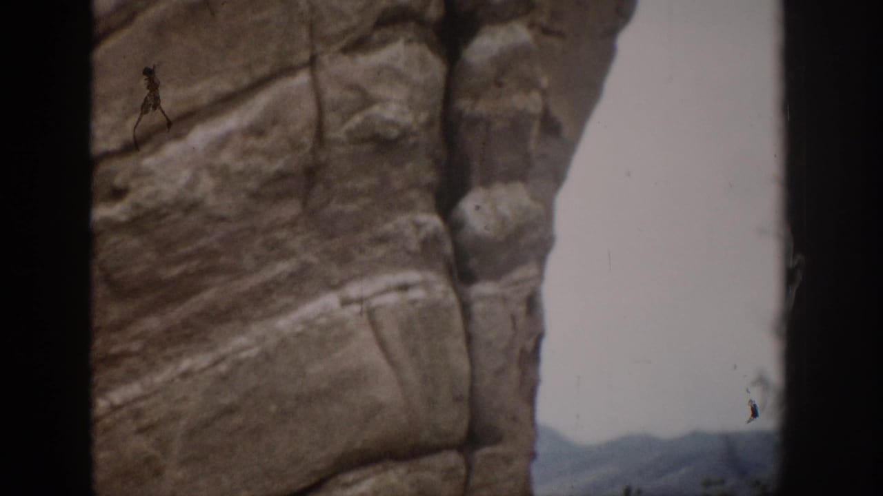 1959 Colorado 8mm frame with a textured vertical rock formation and distant mountain shapes near the frame edge.
