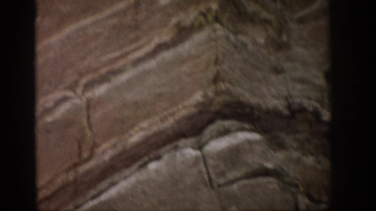 1959 Colorado home-movie frame showing a close view of rough layered rock with natural cracks and dark 8mm frame edges.