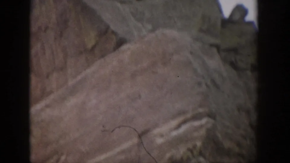 Close 8mm view of a Colorado rock face, with pale layered stone, surface cracks, and heavy frame-edge shadow.