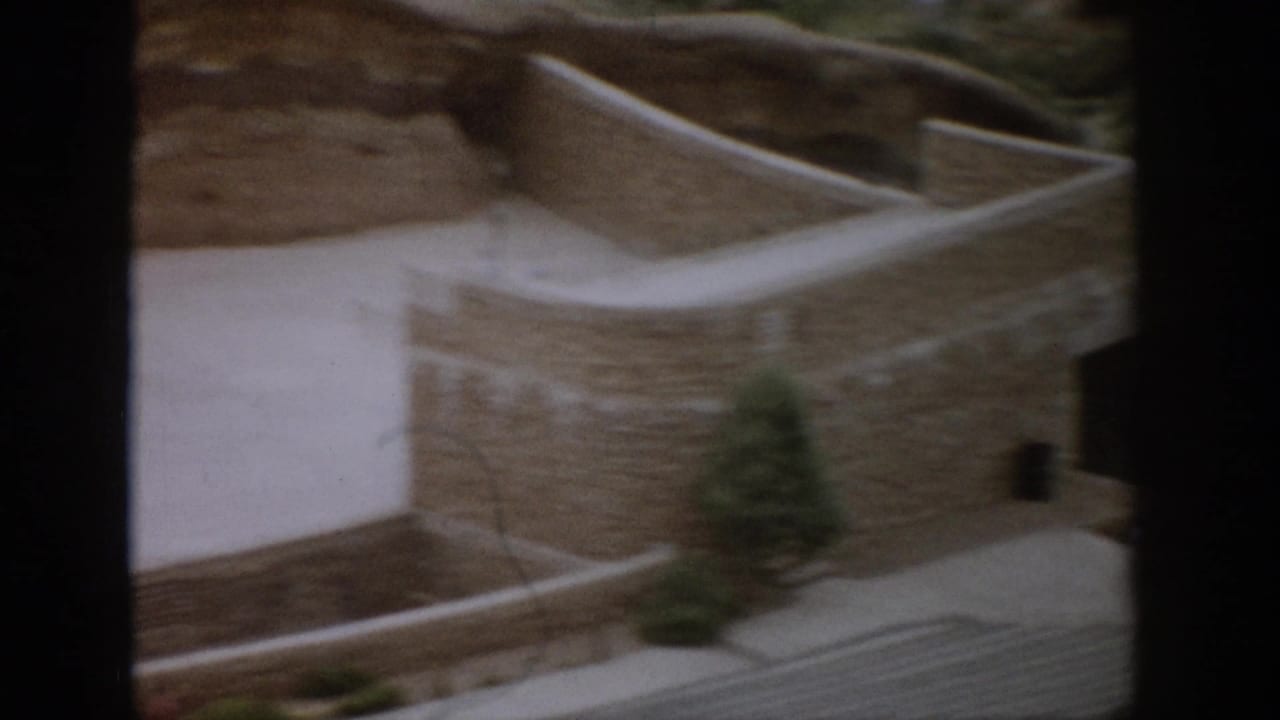 Curved stone walls and a pale concrete walkway beside a rocky hillside.