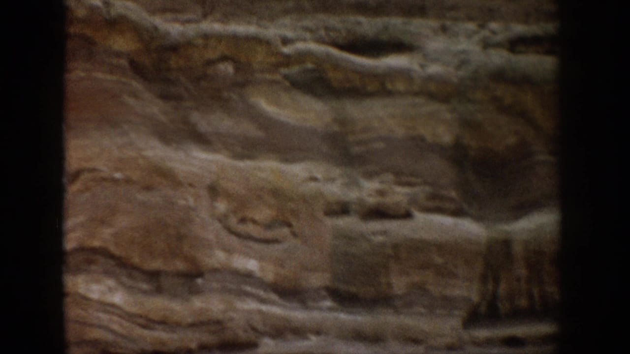 1959 Colorado home-movie frame showing a layered canyon rock wall in soft focus with dark 8mm frame edges.