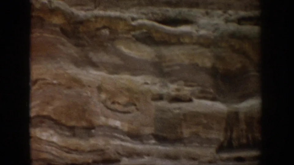 1959 Colorado home-movie frame showing a layered canyon rock wall in soft focus with dark 8mm frame edges.