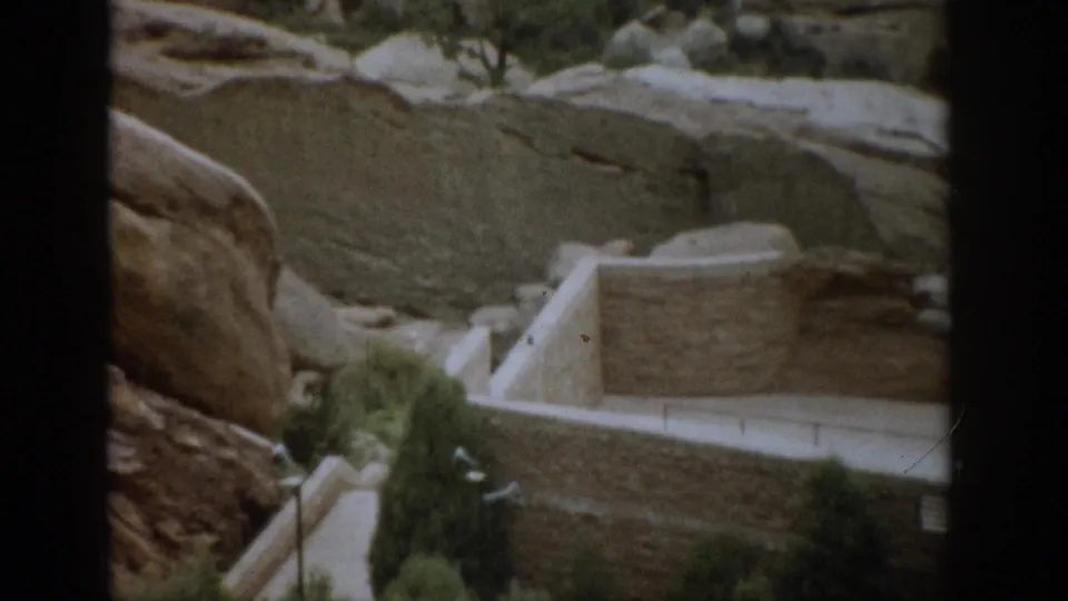 1959 Colorado sightseeing frame showing a stone retaining structure, walkway, shrubs, and surrounding canyon rock.