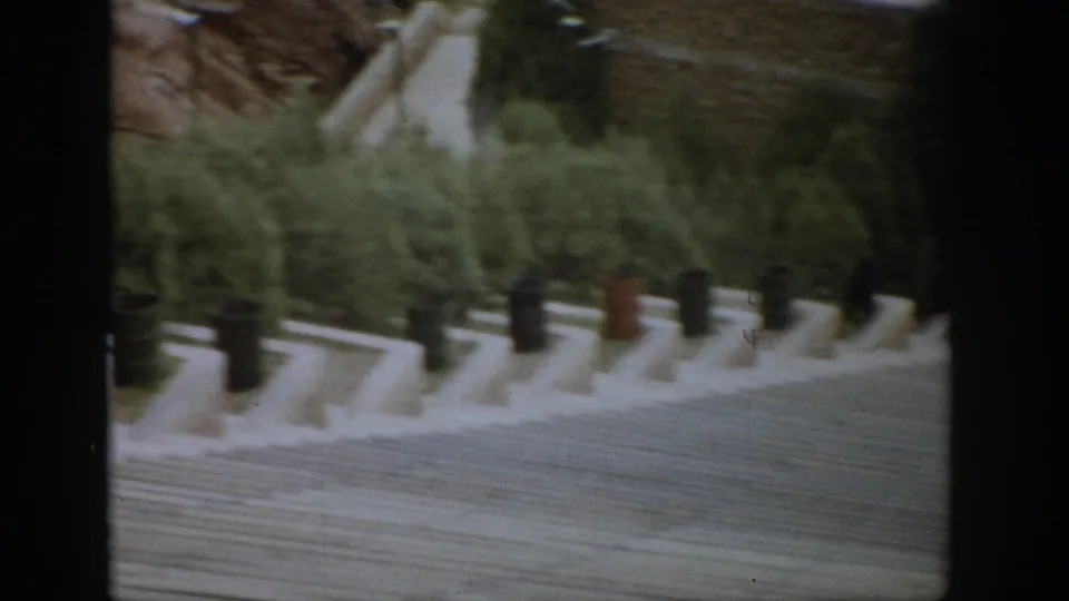 1959 Colorado 8mm frame showing a wide hillside staircase lined with green and brown barrels, with evergreen plantings in the background.