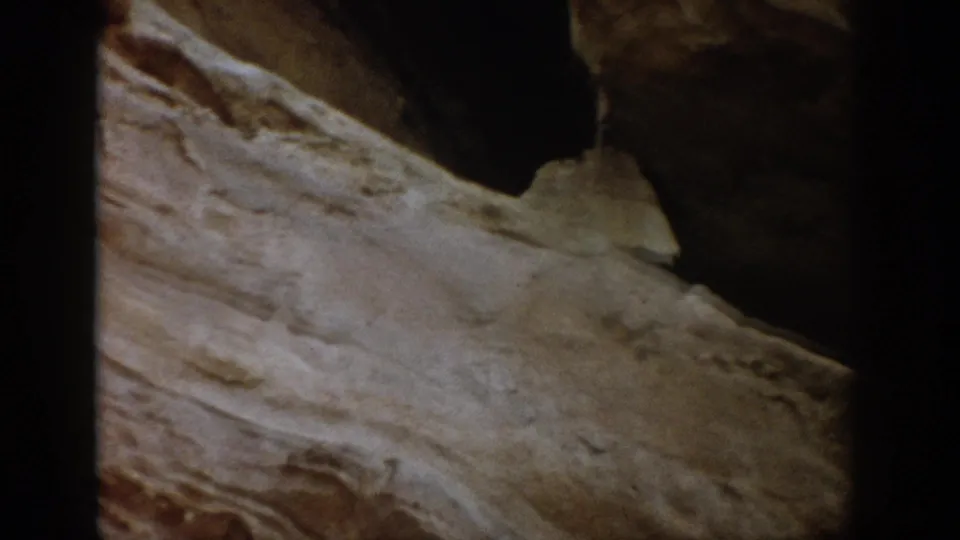 1959 Colorado 8mm frame showing layered rock textures and a dark hollow, with warm color and soft home-movie focus.