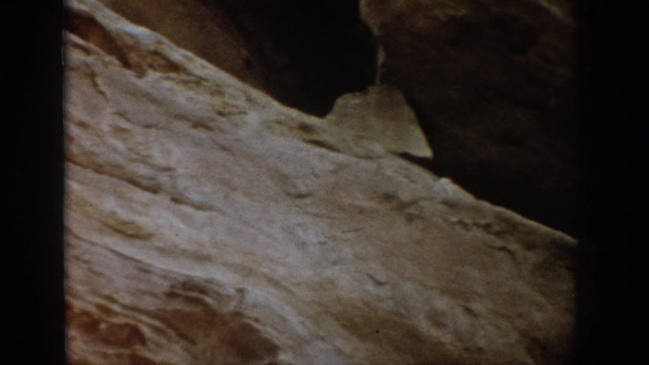 1959 Colorado 8mm frame showing close, textured stratified rock with dark recesses and visible home-movie edge framing.