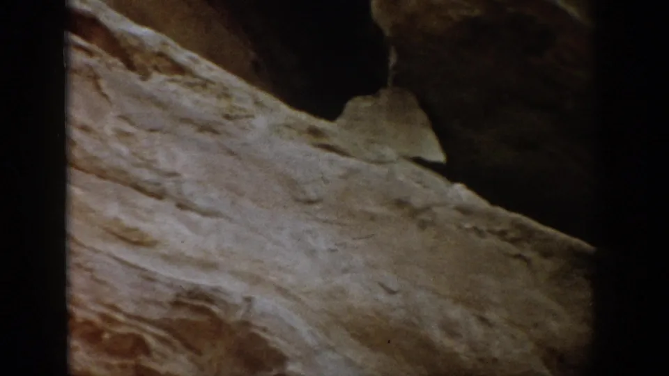 1959 Colorado 8mm frame showing close, textured stratified rock with dark recesses and visible home-movie edge framing.