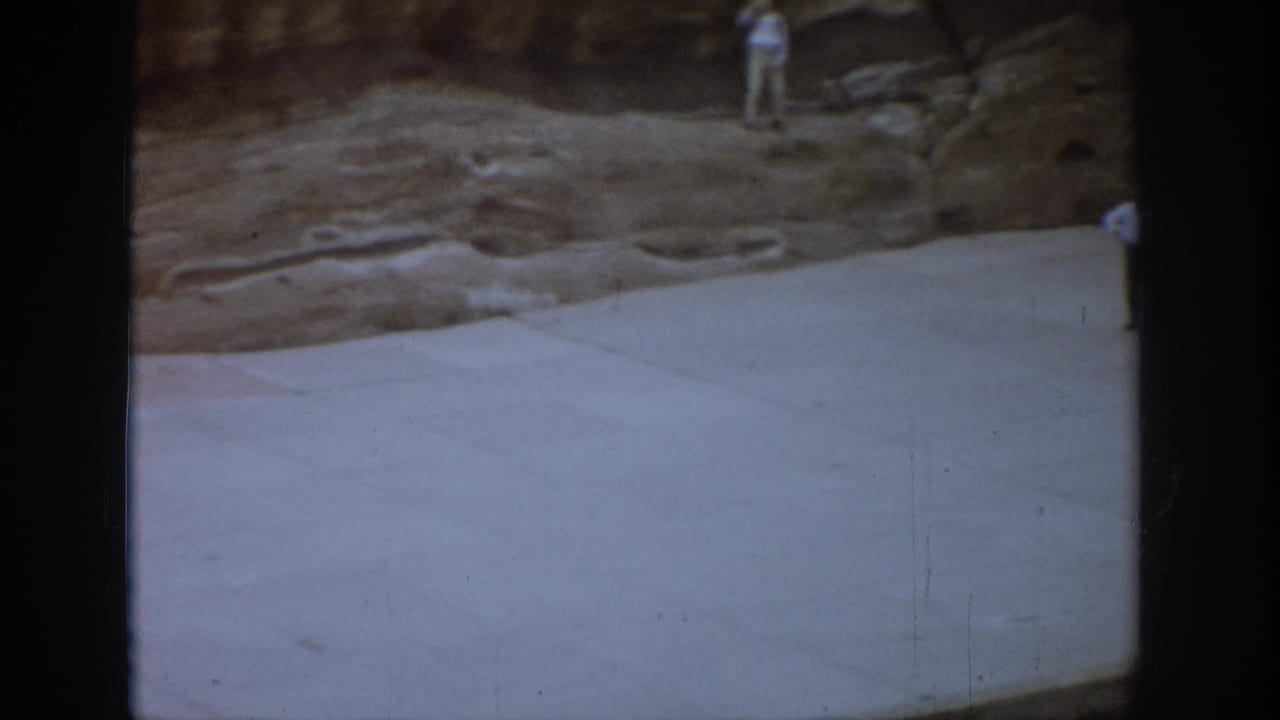 Wide pale platform below a rock wall with a distant person standing near the cliff face.