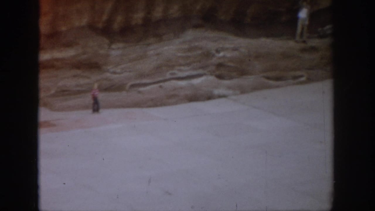 Wide amphitheater floor with a small figure near a rocky wall.