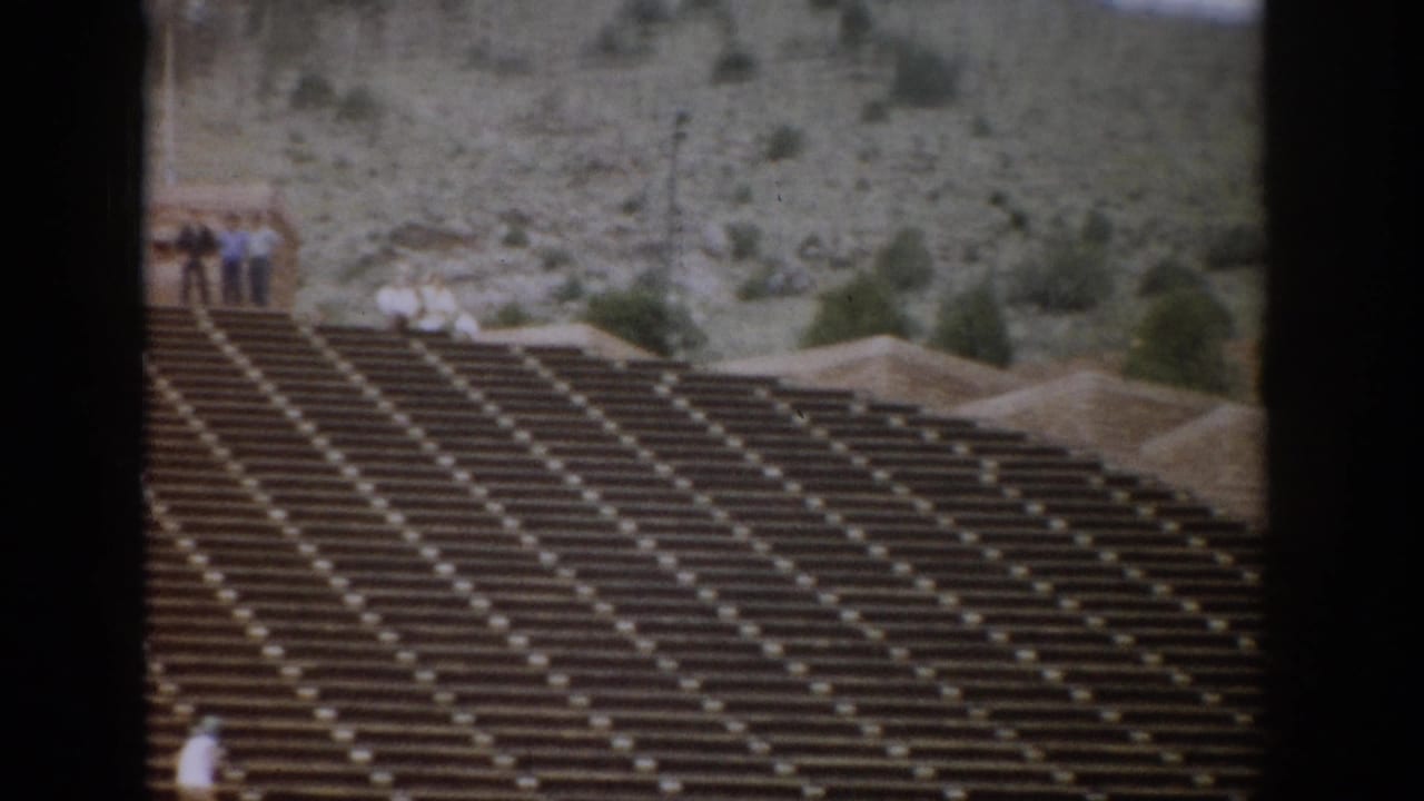 Colorado amphitheater seating in a 1959 home-movie frame, with small groups of tourists near the upper walkway and rocky hillside.