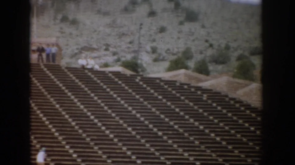 Colorado amphitheater seating in a 1959 home-movie frame, with small groups of tourists near the upper walkway and rocky hillside.