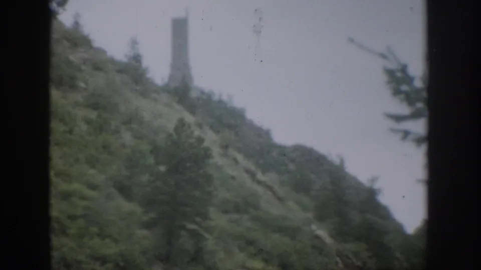 Colorado hillside in 1959 8mm footage, showing shrubs, trees, and a distant tower-like structure partly softened by focus and exposure.