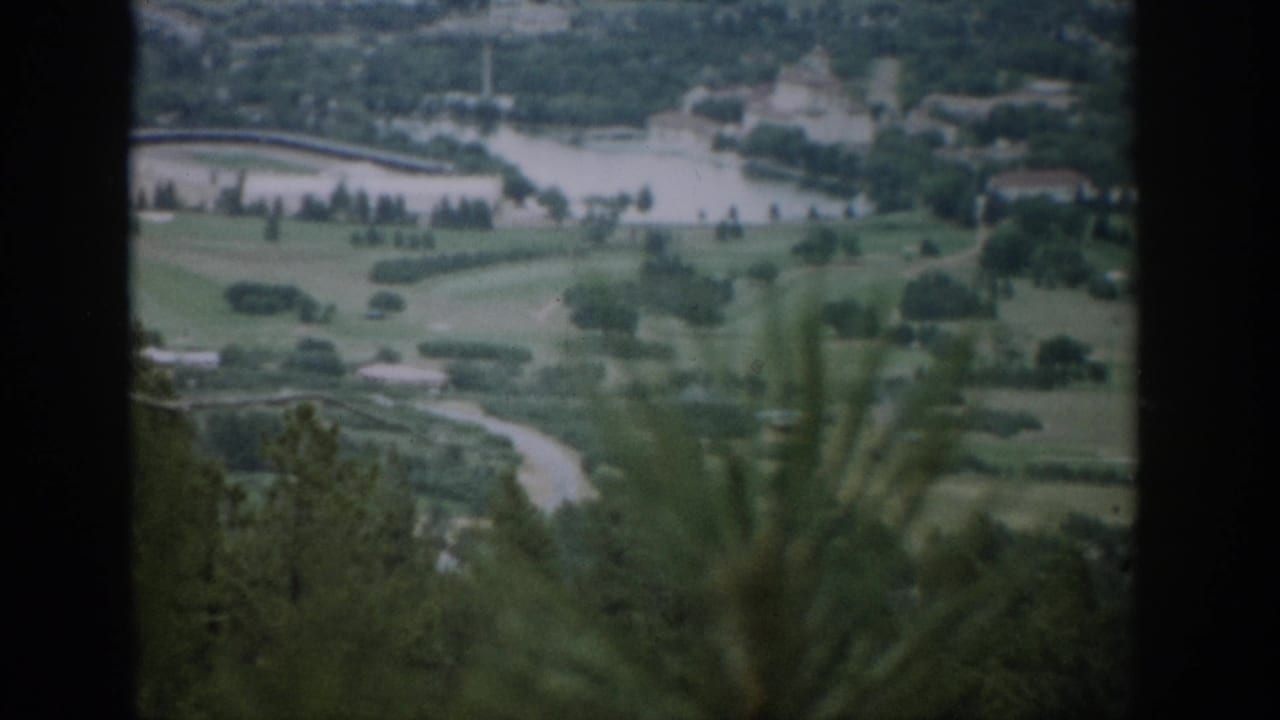 Elevated view of green grounds, water, roads, and trees beyond a dark frame.