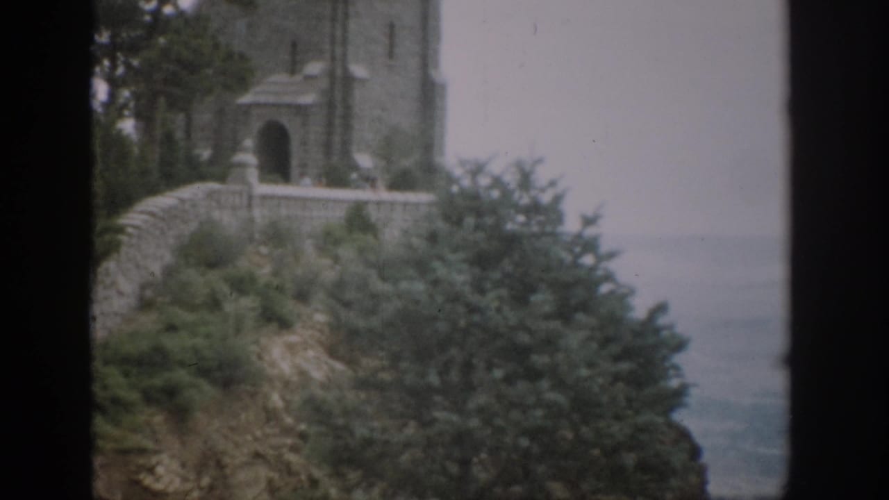 1959 Colorado 8mm frame showing a stone tower, arched doorway, masonry wall, greenery, and hazy horizon.