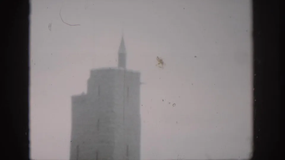Soft 1959 Colorado home-movie frame of a stone tower and pointed spire divided by dark window mullions.