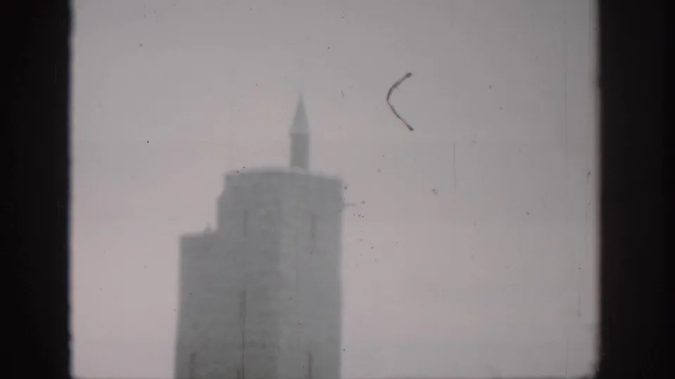 Hazy 8mm frame from Colorado in 1959 showing part of a stone tower with a pointed spire beyond a window opening.