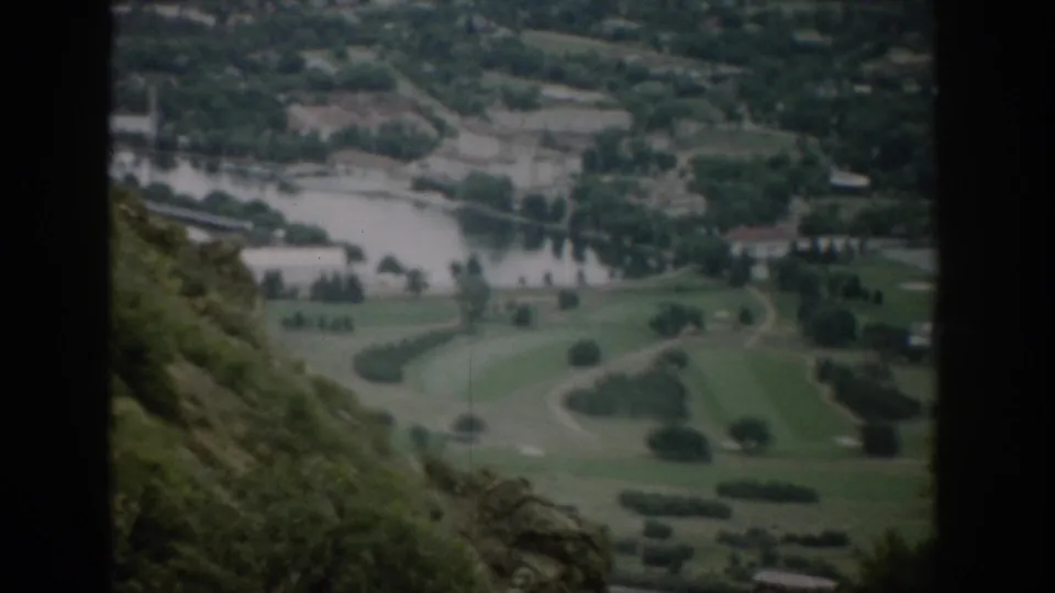 1959 Colorado 8mm frame showing an elevated view of a small town valley with river, green fields, roads, and scattered buildings.