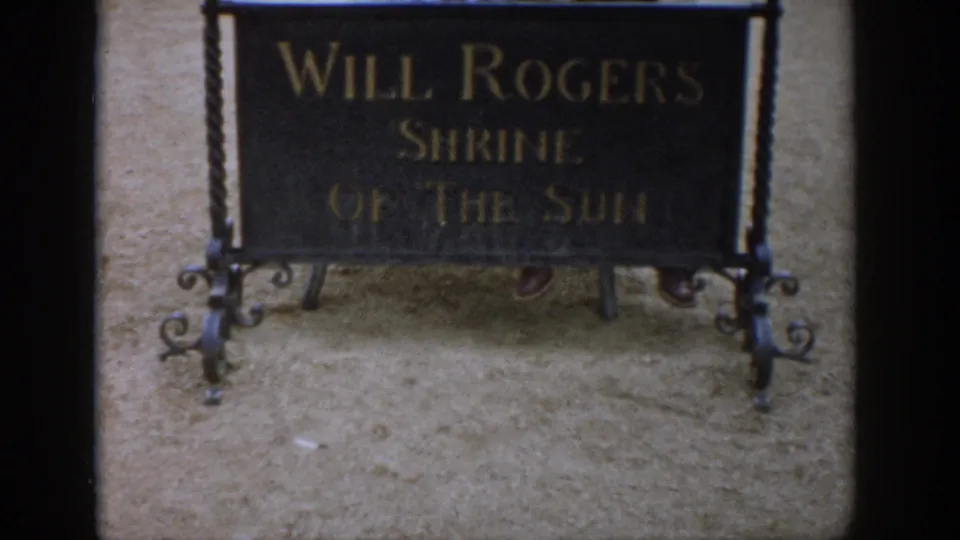 Handheld 8mm view of the Will Rogers Shrine of the Sun sign in Colorado, with ornate metalwork and gravel below.