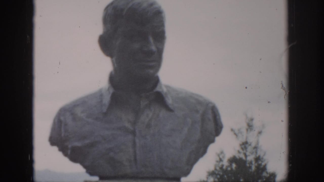 Stone bust of a man in a collared shirt, framed against trees and pale sky.