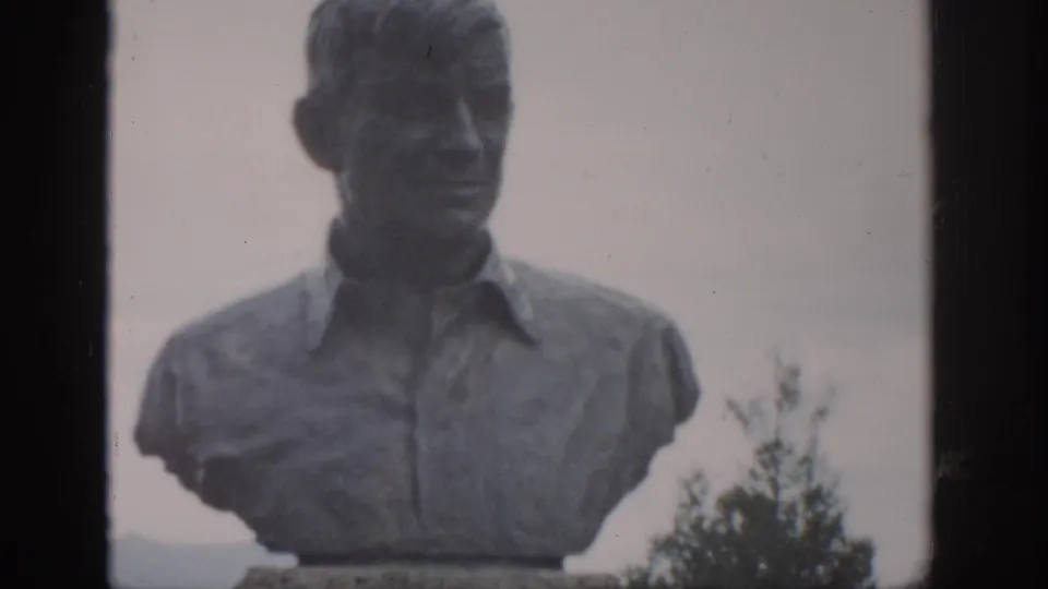 1959 Colorado 8mm frame showing a closer visitor-shot view of the stone bust, with soft focus, trees, and distant hills in the background.