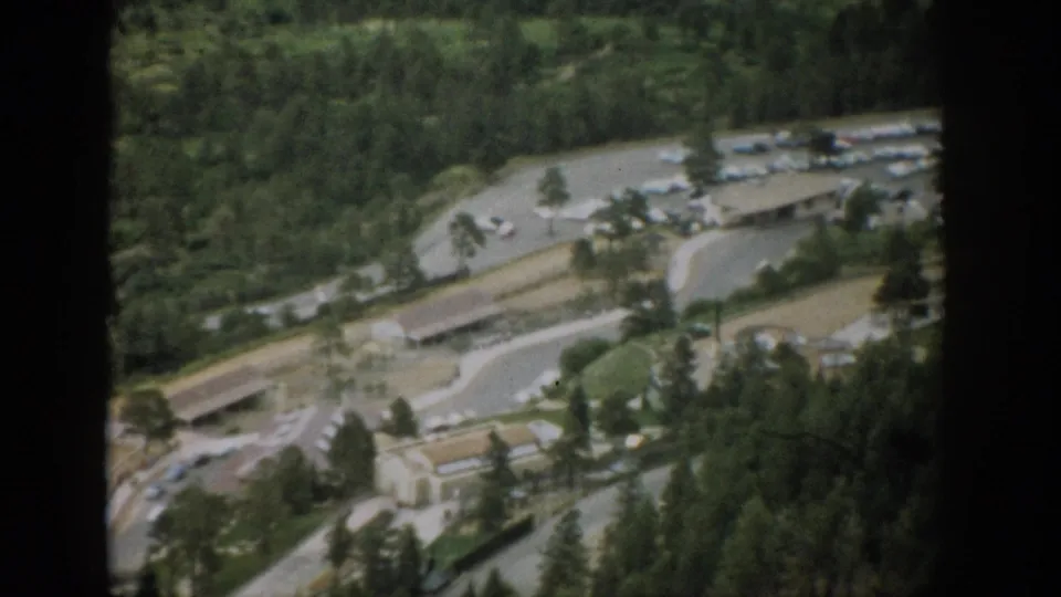 1959 Colorado 8mm frame with a soft high-angle view of roads, a parking area, small buildings, and pine forest through a window divider.