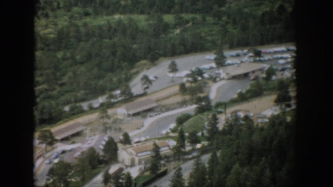 1959 Colorado 8mm frame showing a winding mountain road, small roadside facility, parked cars, and forested slopes from above.