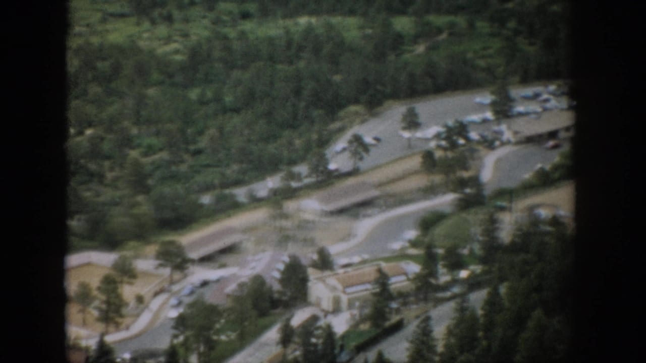 High view of winding roads, a parking lot, low structures, cars, and surrounding trees.
