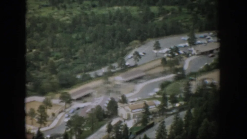 Aerial 1959 Colorado view of winding roads, a roadside facility, parking areas, and trees in a mountain setting.