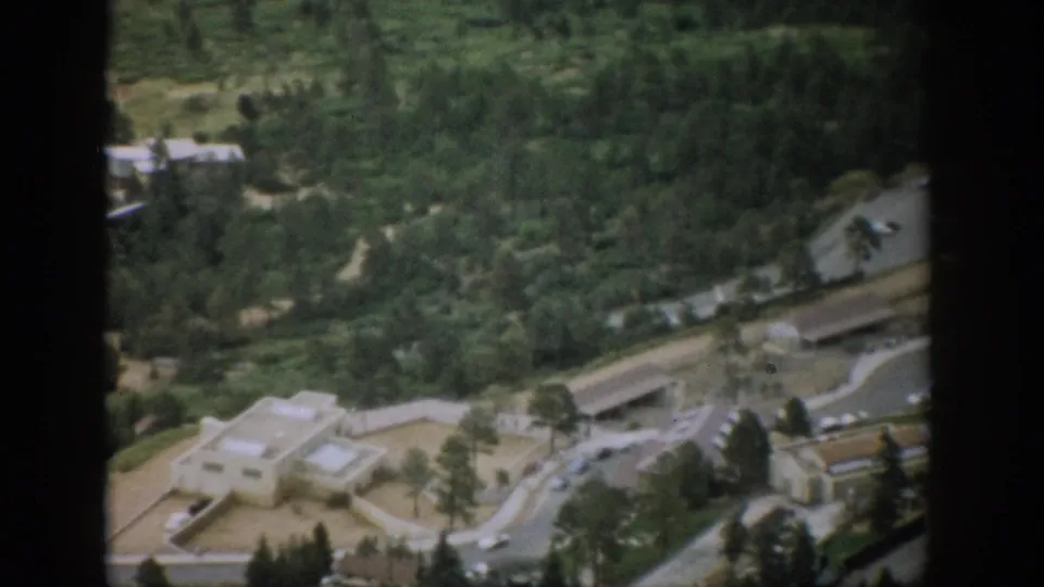 1959 Colorado home-movie aerial view of a roadside complex beside winding roads and forest, with parked cars visible.