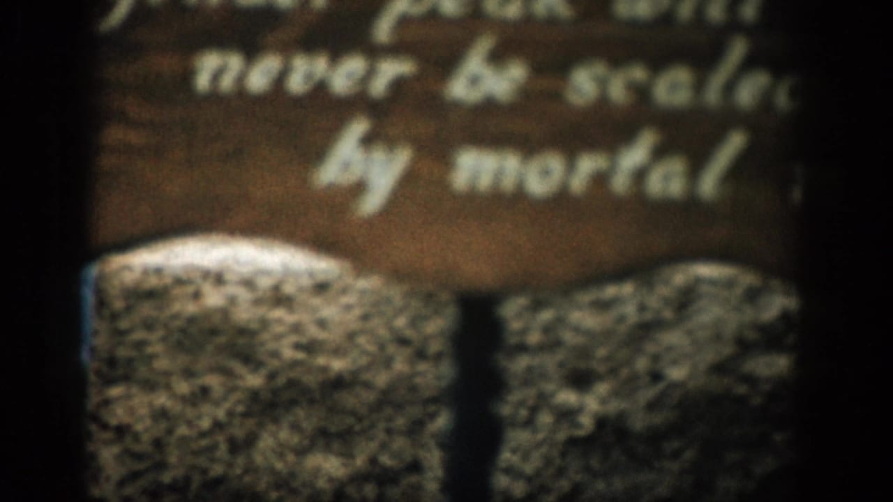 Soft close-up of a wooden sign above rough stone with partially readable white lettering.