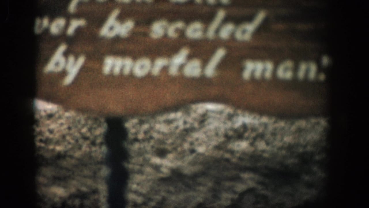 1959 Colorado 8mm frame showing a soft-focus wooden sign with white text in front of rugged mountain terrain.
