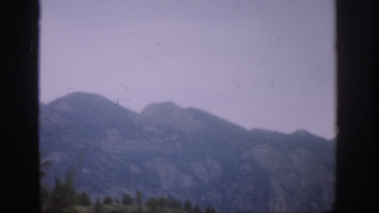 Distant mountain ridge seen through dark vertical frame bars under a hazy sky.